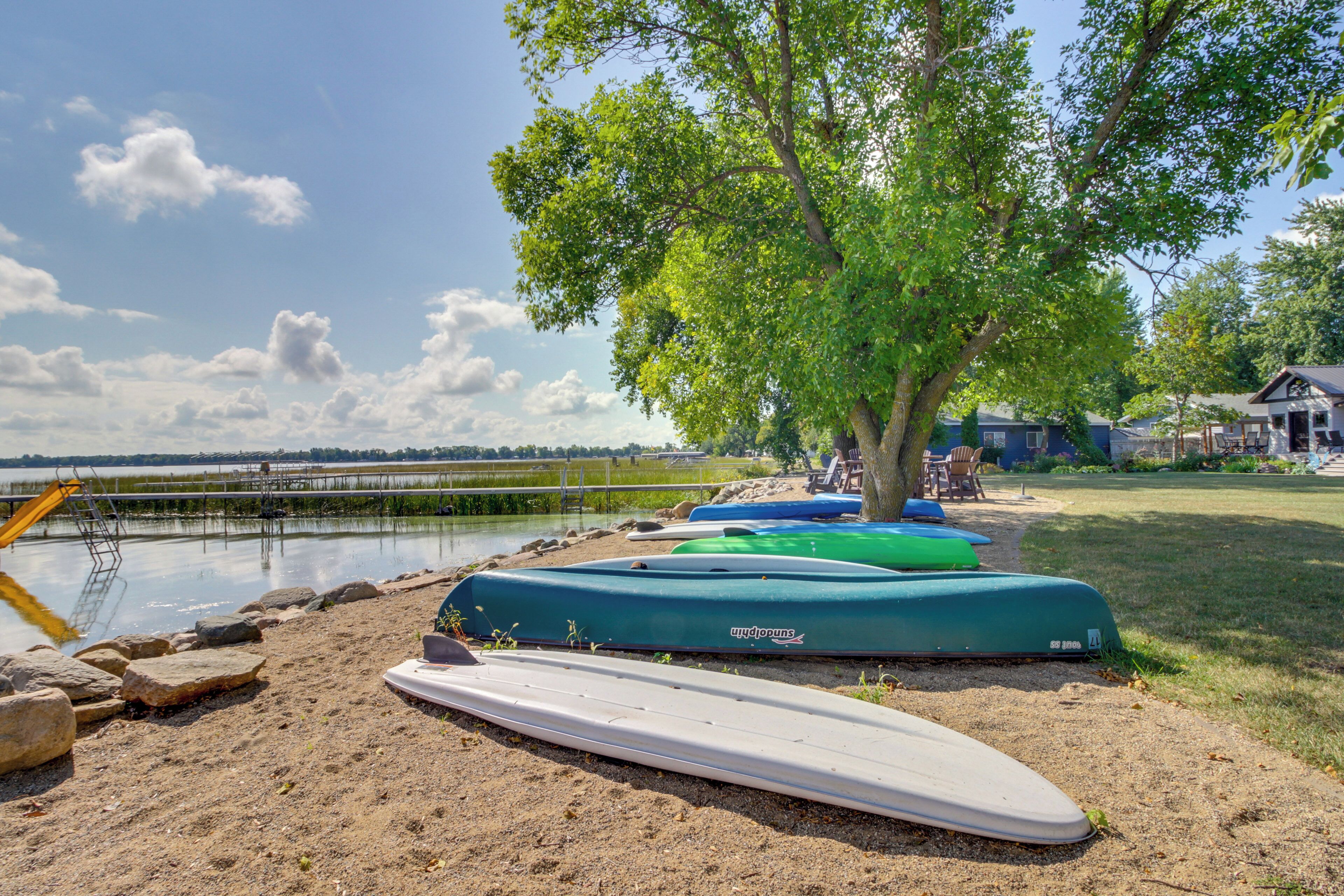 A lakeside setting with kayaks and a paddleboard near a dock.