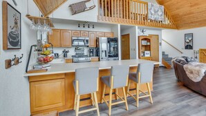 A spacious kitchen with wooden cabinets, a central island with bar stools, a microwave, and a refrigerator. - Angel Fire Retreat w/ Hot Tub ~ 5 Mi to Skiing (Angel Fire)