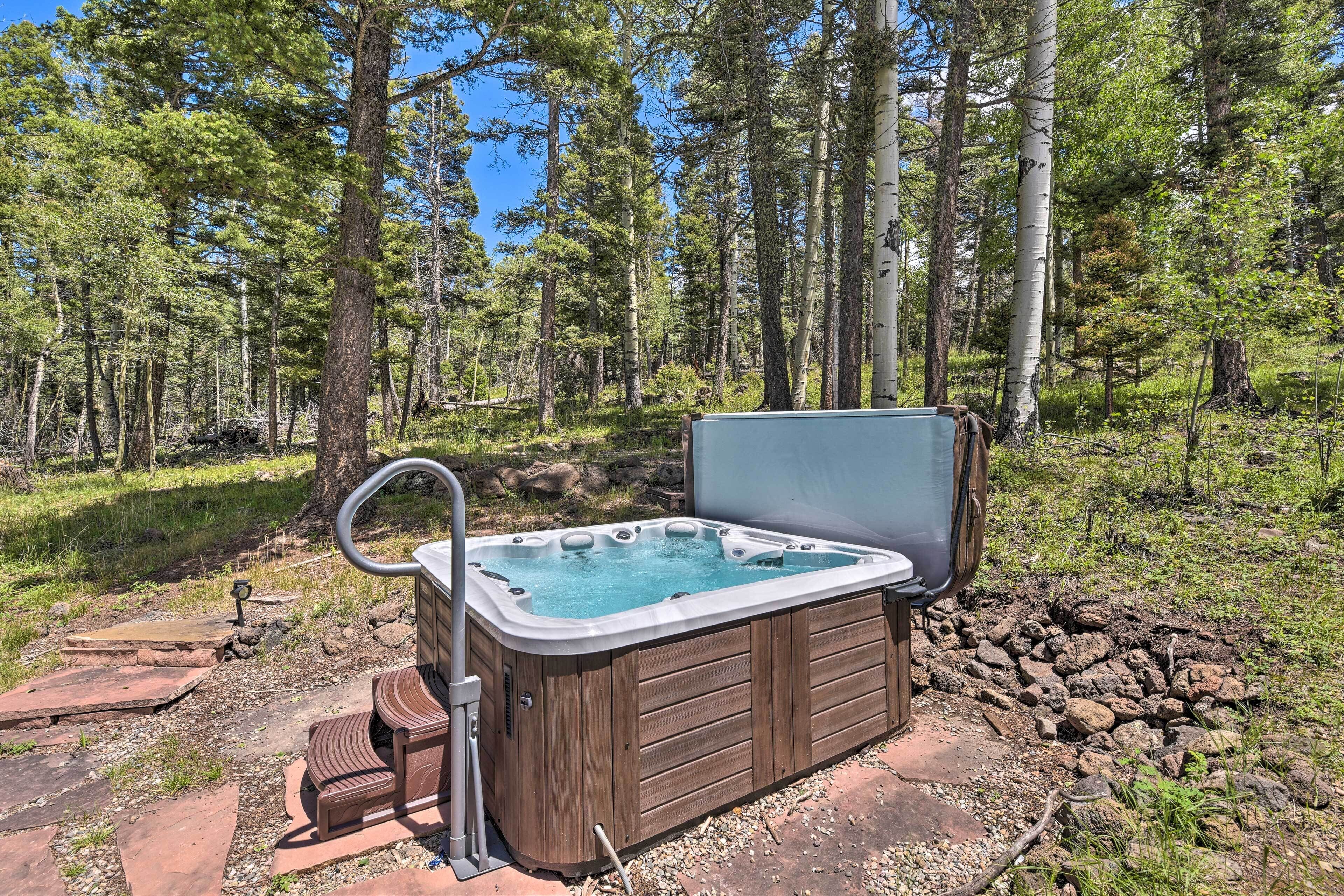 A hot tub in a forested area with a wooden deck and steps leading up to it.