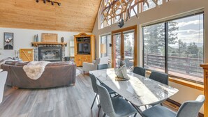 A spacious living room with a fireplace, a dining table, and large windows offering a view of the outdoors. - Angel Fire Retreat w/ Hot Tub ~ 5 Mi to Skiing (Angel Fire)