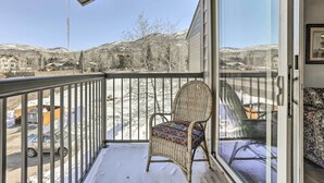 Ein Balkon mit einem Korbstuhl, Blick auf eine verschneite Landschaft und ein Gebäude im Hintergrund.