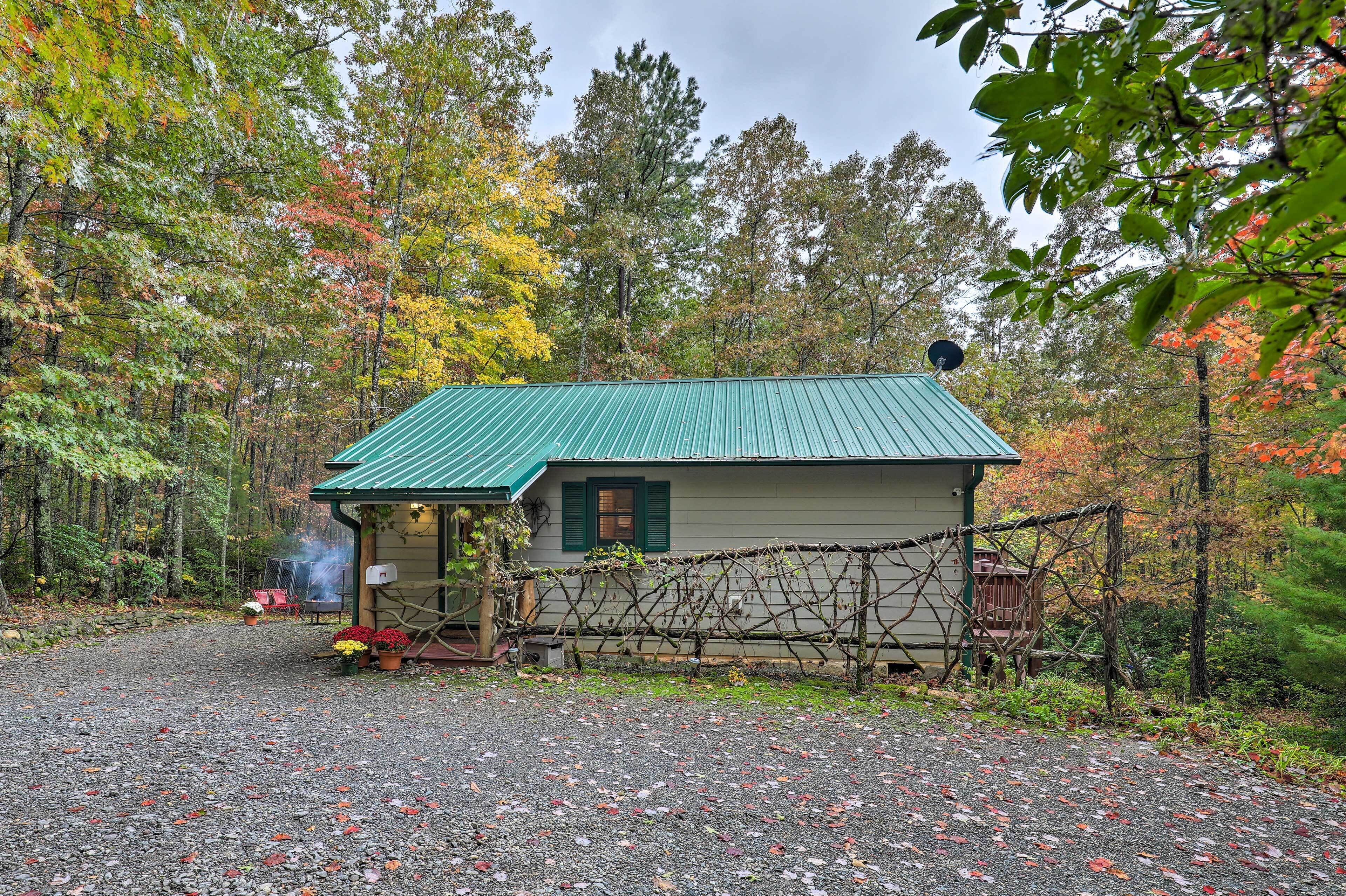 A cabin with a green roof, surrounded by a gravel driveway and a wooden fence.