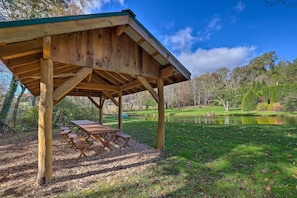 A wooden pavilion with picnic tables, a pond, and a grassy area with trees in the background. - Fletcher Cabin: Wraparound Deck & Pond Access (Fletcher)