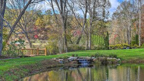 A pond with a small waterfall, surrounded by trees and a wooden bridge. - Fletcher Cabin: Wraparound Deck & Pond Access (Fletcher)