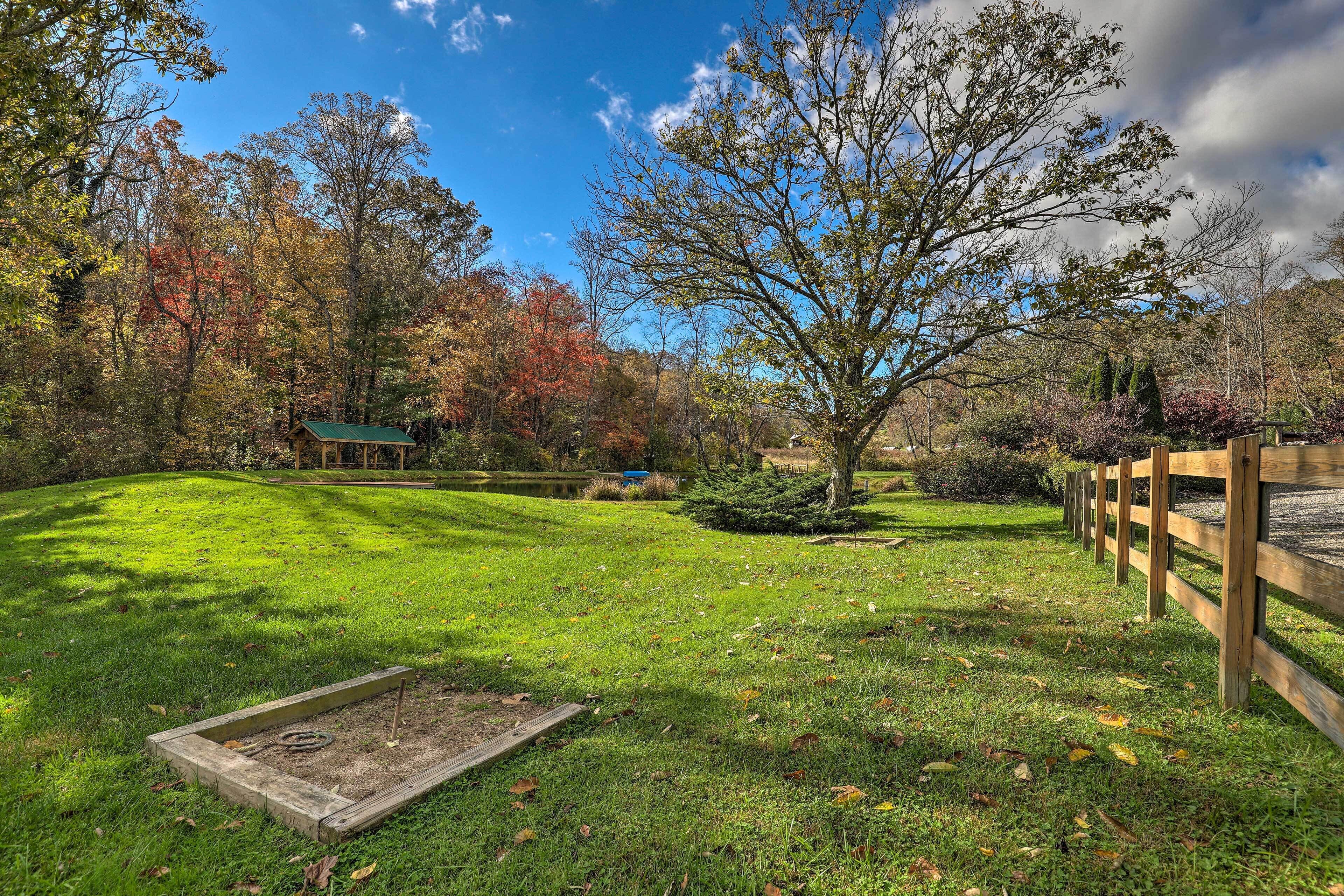 A grassy area with a wooden fence, a small shed, and trees with autumn foliage.