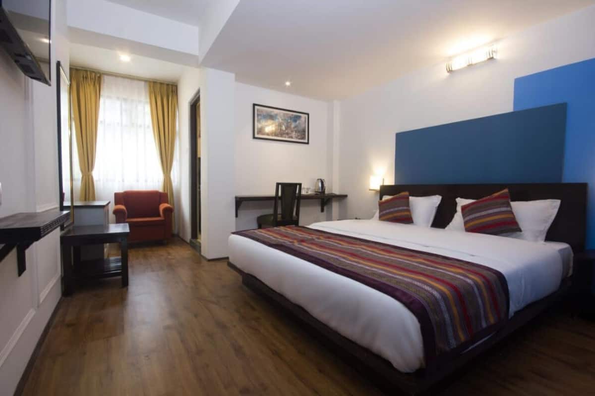 A hotel room with a large bed, a desk, a chair, and a window with curtains.