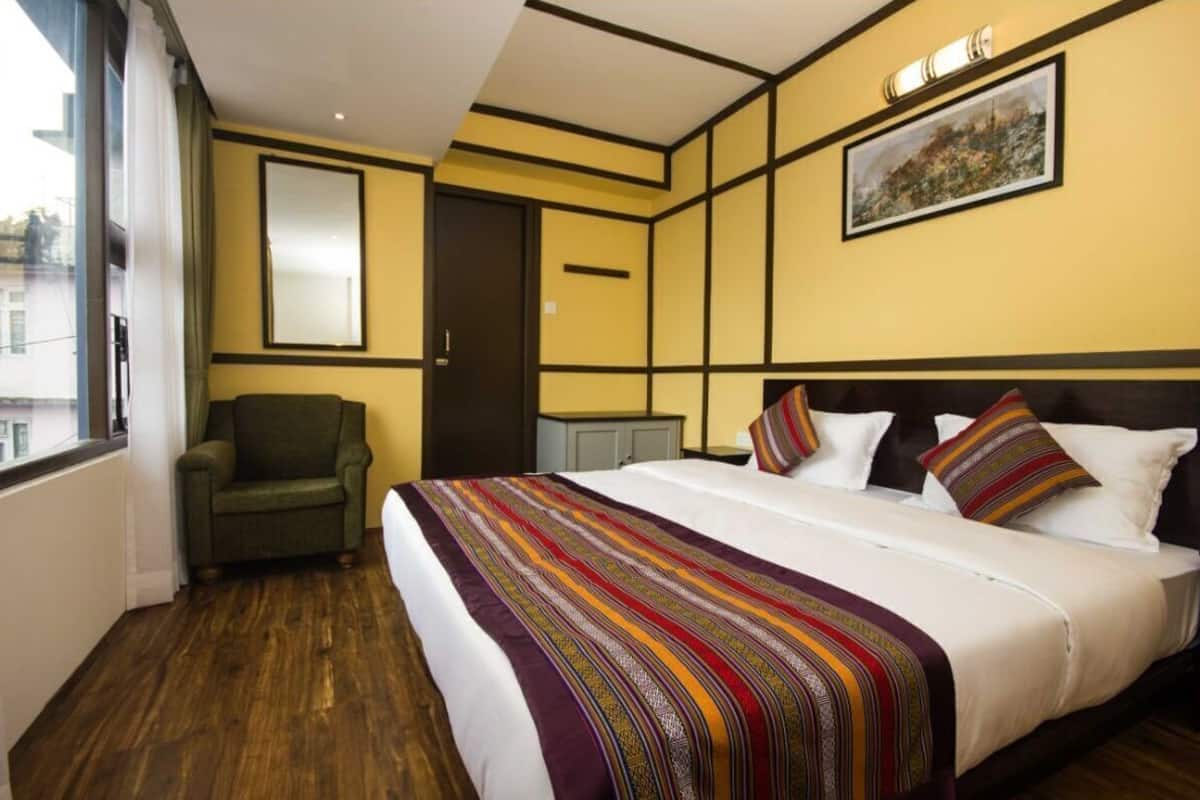 A hotel room with a large bed, a chair, a wardrobe, and a painting on the wall.
