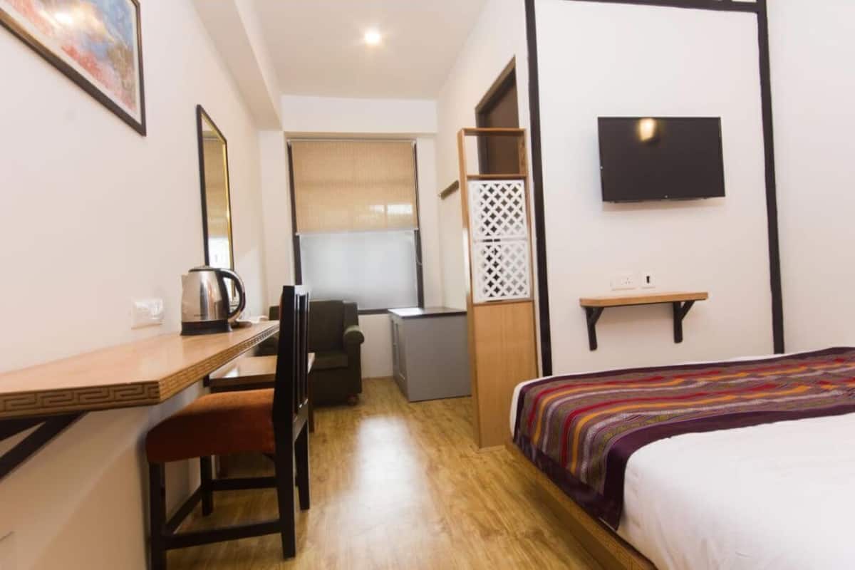 A compact hotel room with a bed, a desk, a chair, a TV, and a small kitchenette.