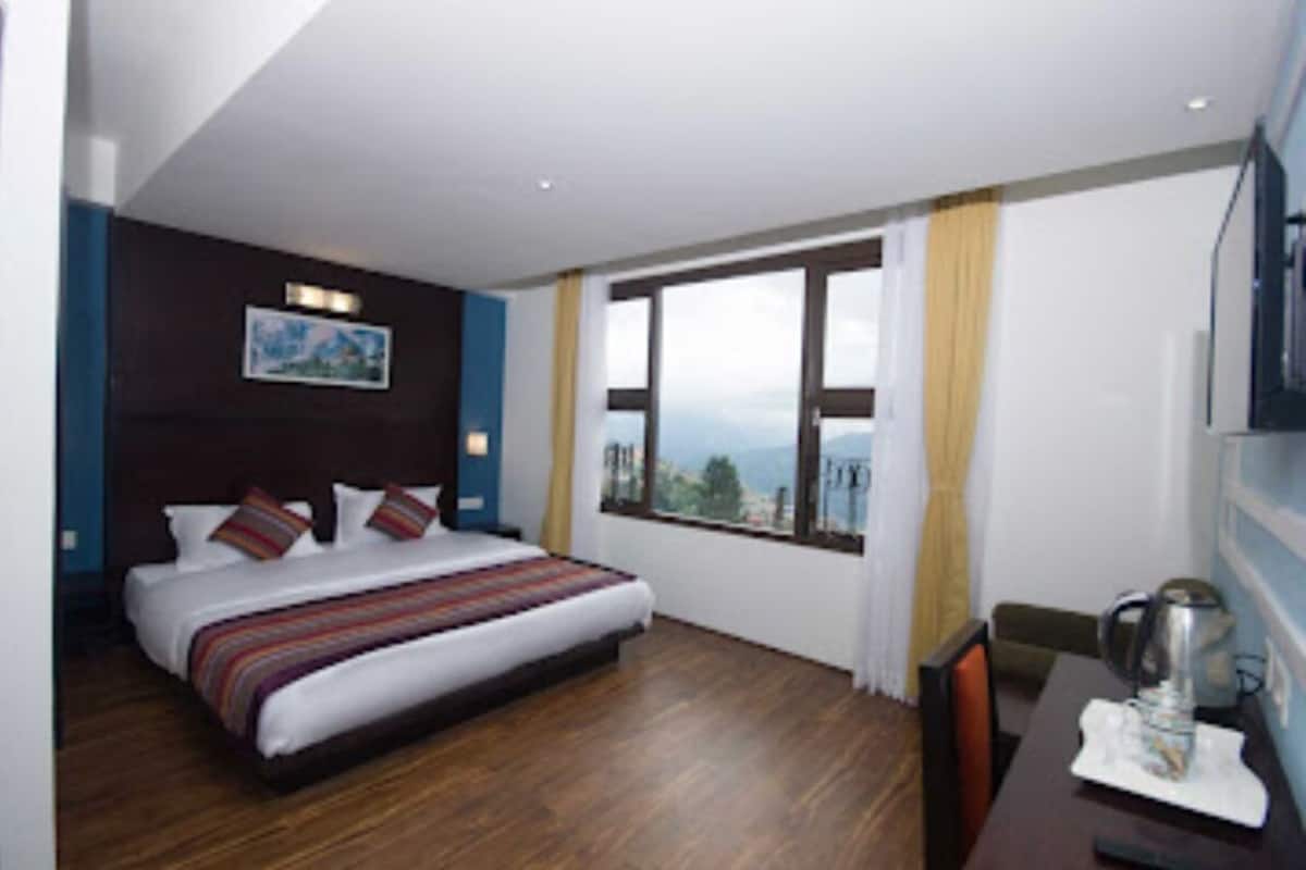 A hotel room with a large bed, a dining table, and a view of the mountains.