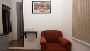 A room with a wooden floor, a red armchair, a small table, a framed picture on the wall, and a window with a blind. - Bumble Bee (Gangtok)
