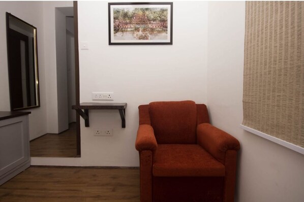 A room with a wooden floor, a red armchair, a small table, a framed picture on the wall, and a window with a blind.