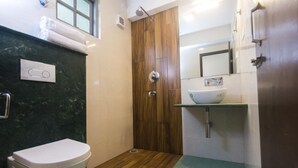 A compact bathroom with a white toilet, a wooden door, a white sink with a mirror above it, and a green mat on the floor. - Bumble Bee (Gangtok)