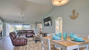 A spacious living area with a brown leather sectional sofa, a wooden dining table set with blue bowls and glasses, and a large anchor decoration on the wall. - 15 Mi to Beach: Home w/ Pool in Cape Coral (Cape Coral)
