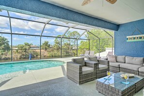 Un espace aménagé au bord de la piscine, avec des meubles en osier, une table en verre et un panneau indiquant « PLAGE ».