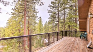 A wooden deck with a glass railing, overlooking a forest of tall pine trees.