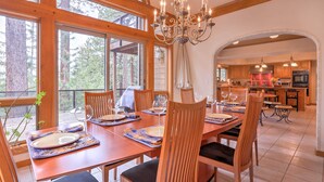 A dining area with a wooden table set for four, surrounded by chairs, large windows, and a view of the outdoors.