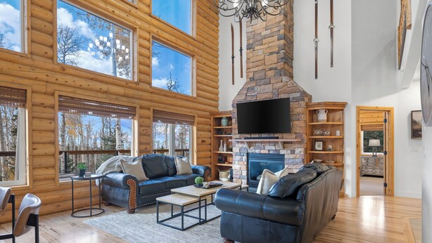A spacious log cabin interior with a stone fireplace, leather sofas, and large windows offering views of the forest. - Spacious Mtn Manor, 1 Mi to Brian Head Resort! (Brian Head)