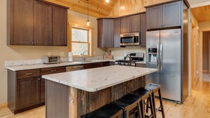 A modern kitchen with wooden cabinets, stainless steel appliances, and a large island with bar stools. - Spacious Cabin: 10 Mi to Sunday River Skiing! (Bethel)