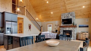 A spacious kitchen with a large island, a stone fireplace, and a dining area with a wooden table. - Spacious Cabin: 10 Mi to Sunday River Skiing! (Bethel)