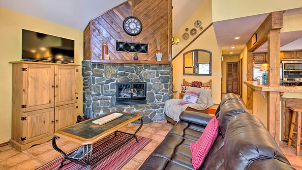 A cozy living room with a stone fireplace, a leather sofa, and a television. - Serene Angel Fire Cabin w/ Community Pools! (Angel Fire)