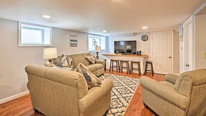 A living room with a sofa set, a patterned rug, a TV, and a kitchen area with stools. - Old Orchard Beach Home w/ Patio: Walk to Beach (Old Orchard Beach)