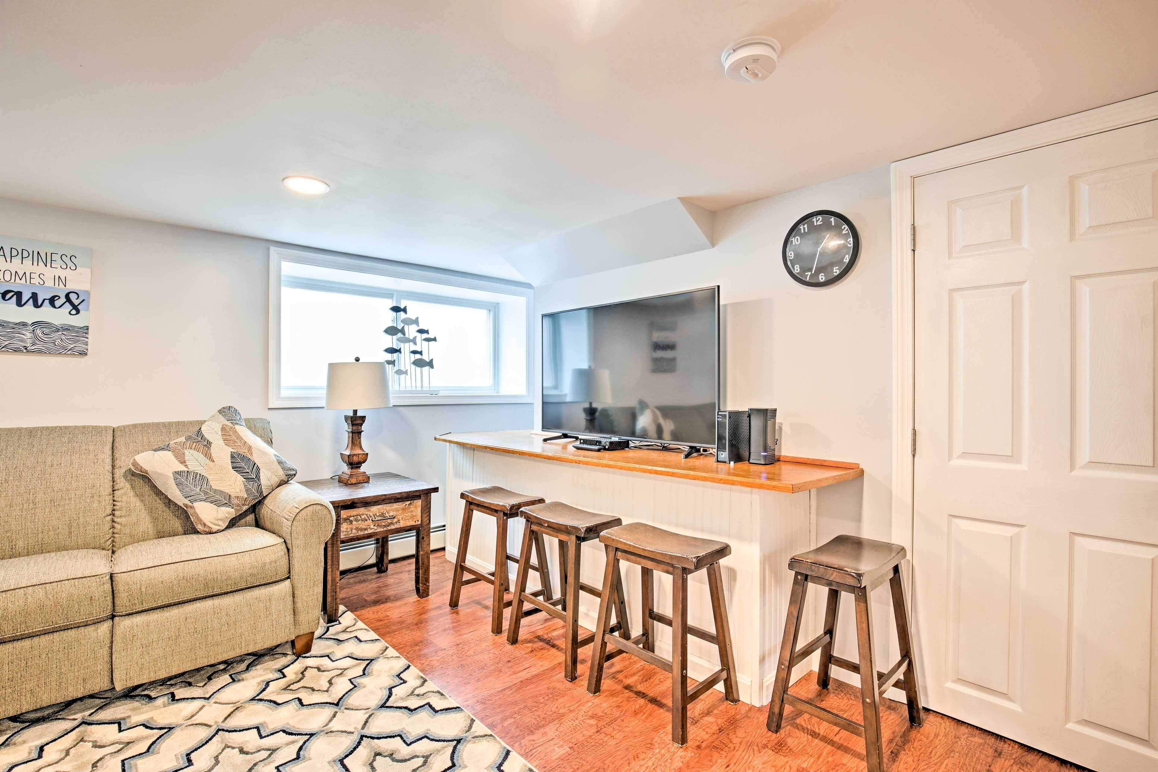 Un espacio habitable compacto con sofá, una mesa de centro, televisor, mostrador de cocina y un taburete de bar.