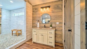 Une salle de bain avec un meuble-lavabo en bois, un miroir rond et un petit tabouret.