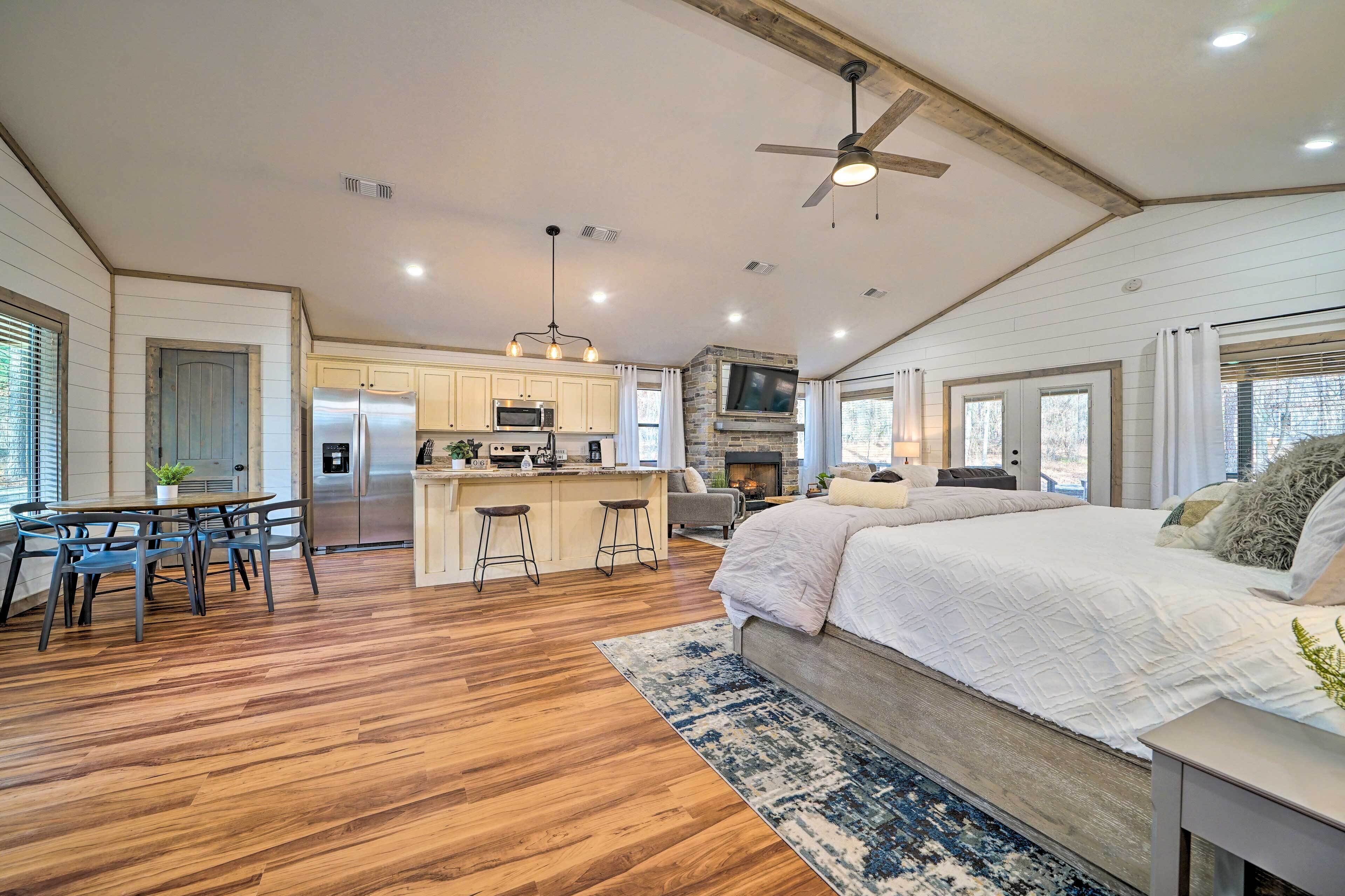 A spacious kitchen with a central island, a dining area with a table and chairs, a large bed with a blue and white patterned rug, and a ceiling fan.