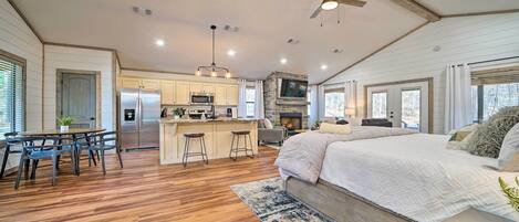 A spacious kitchen with a central island, a dining area with a table and chairs, a large bed with a blue and white patterned rug, and a ceiling fan.