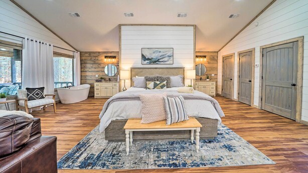 Un dormitorio amplio con una cama grande, una zona de estar con un banco, una bañera y vistas al exterior.