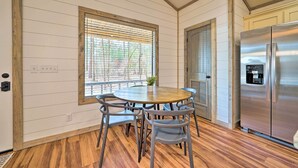 Una cocina con una mesa de madera, sillas, un refrigerador de acero inoxidable y una ventana con persianas.