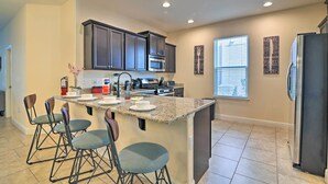 A modern kitchen with dark cabinetry, a granite countertop, and a central island with bar stools.