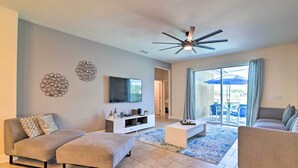 A modern living room with a flat-screen TV, a ceiling fan, and a large sliding glass door leading to an outdoor area.