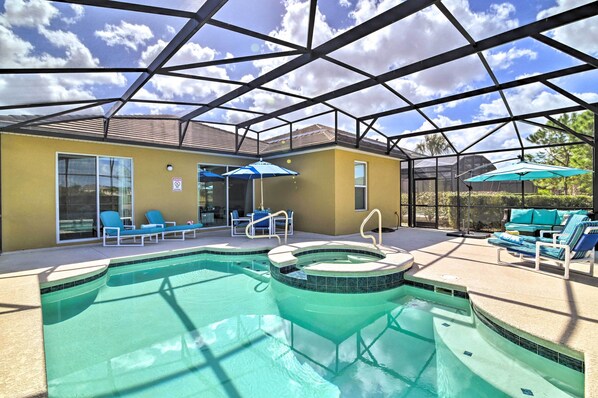 Una piscina interior con jacuzzi, rodeada de sillones de descanso y sombrillas, bajo un techo de vidrio.
