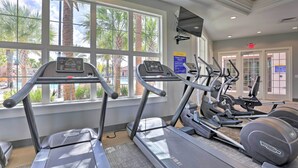 A gym with treadmills, ellipticals, and a stationary bike, large windows with palm trees, and a sign for the fitness center.
