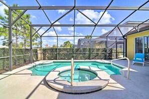 Una piscina exterior cubierta con un jacuzzi, rodeada por una estructura metálica y paneles de vidrio, con vistas a una zona residencial al fondo.
