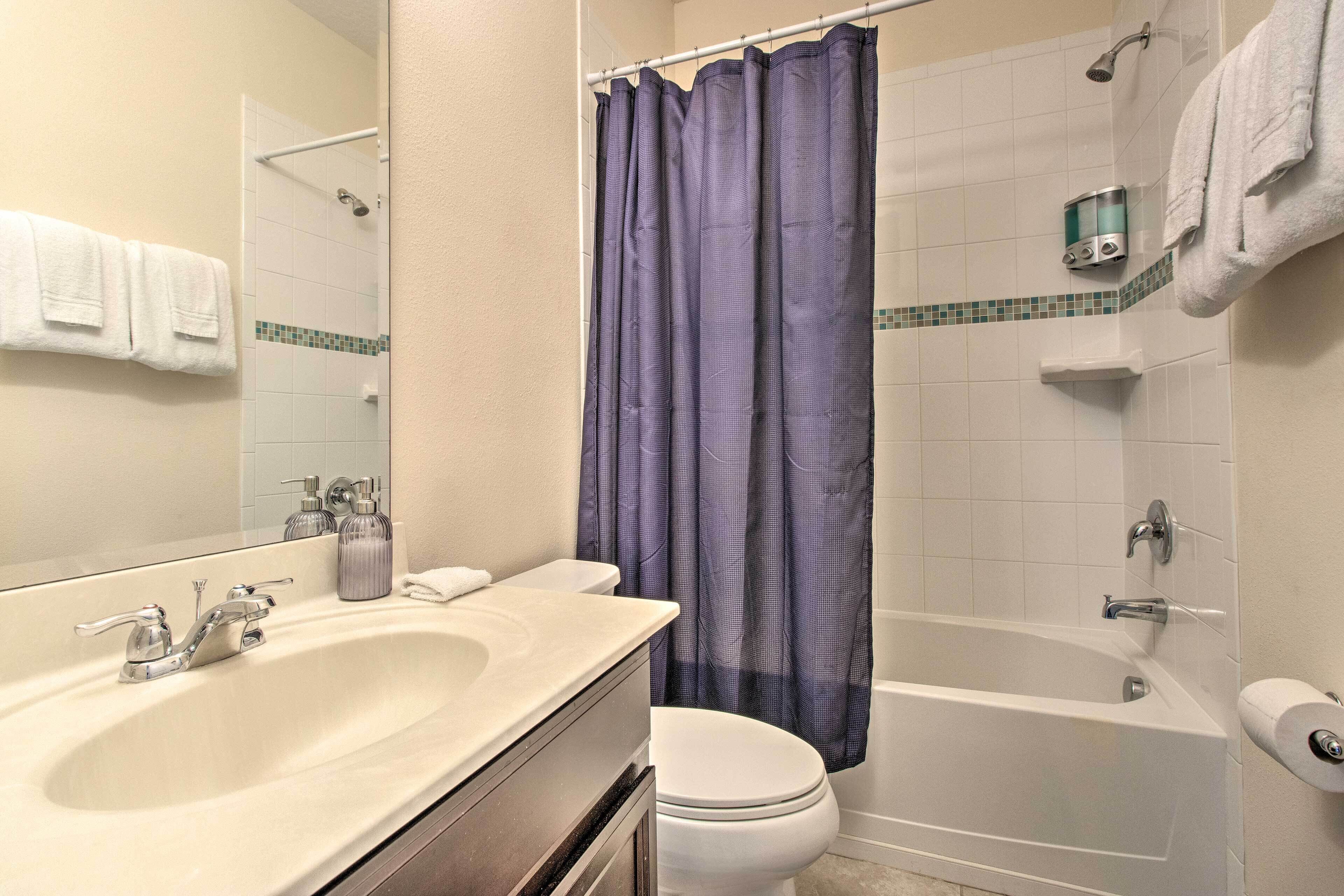 A bathroom with a double sink, toilet, bathtub, and shower curtain.