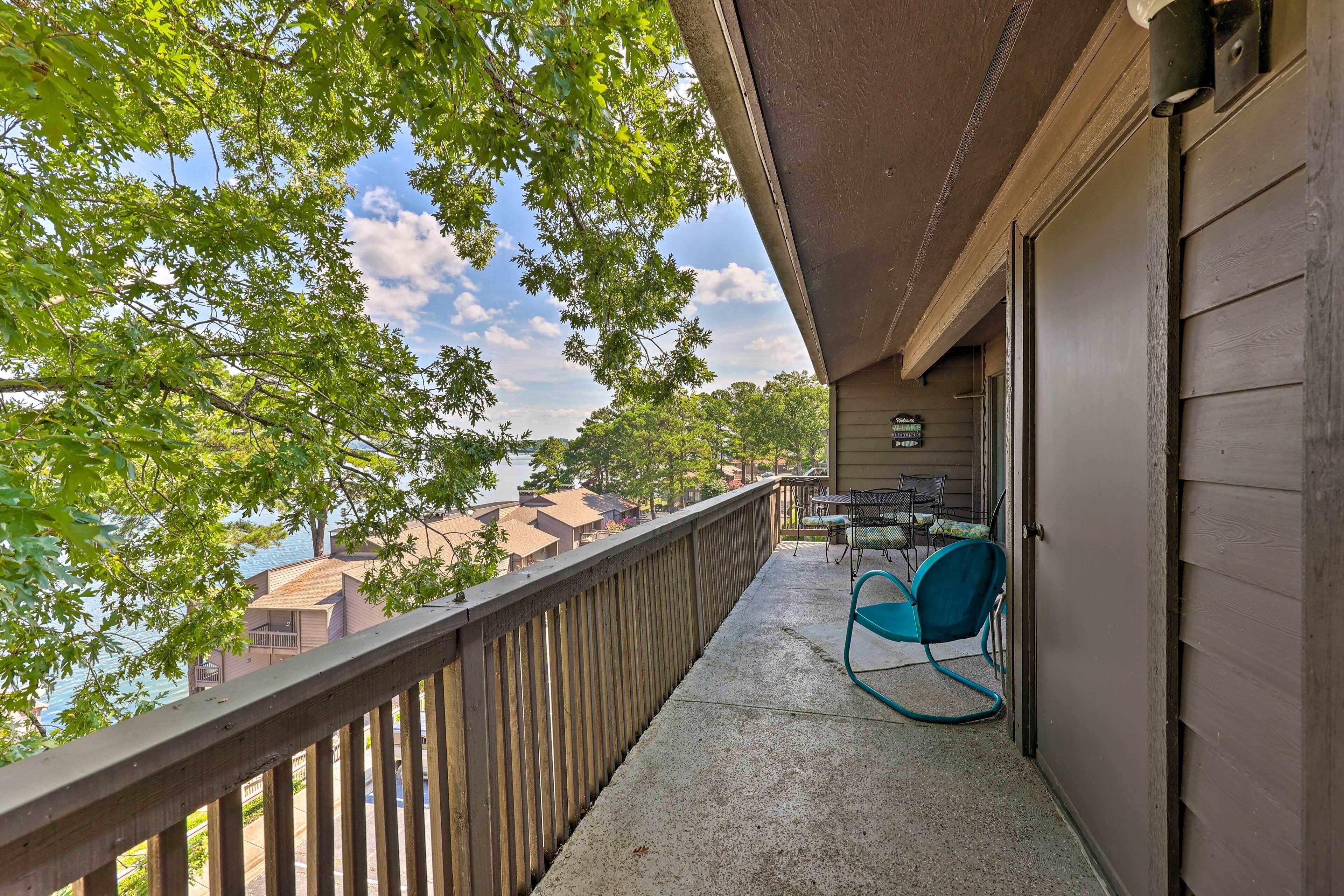 A balcony with a view of a lake, a table with chairs, and a door to a building.