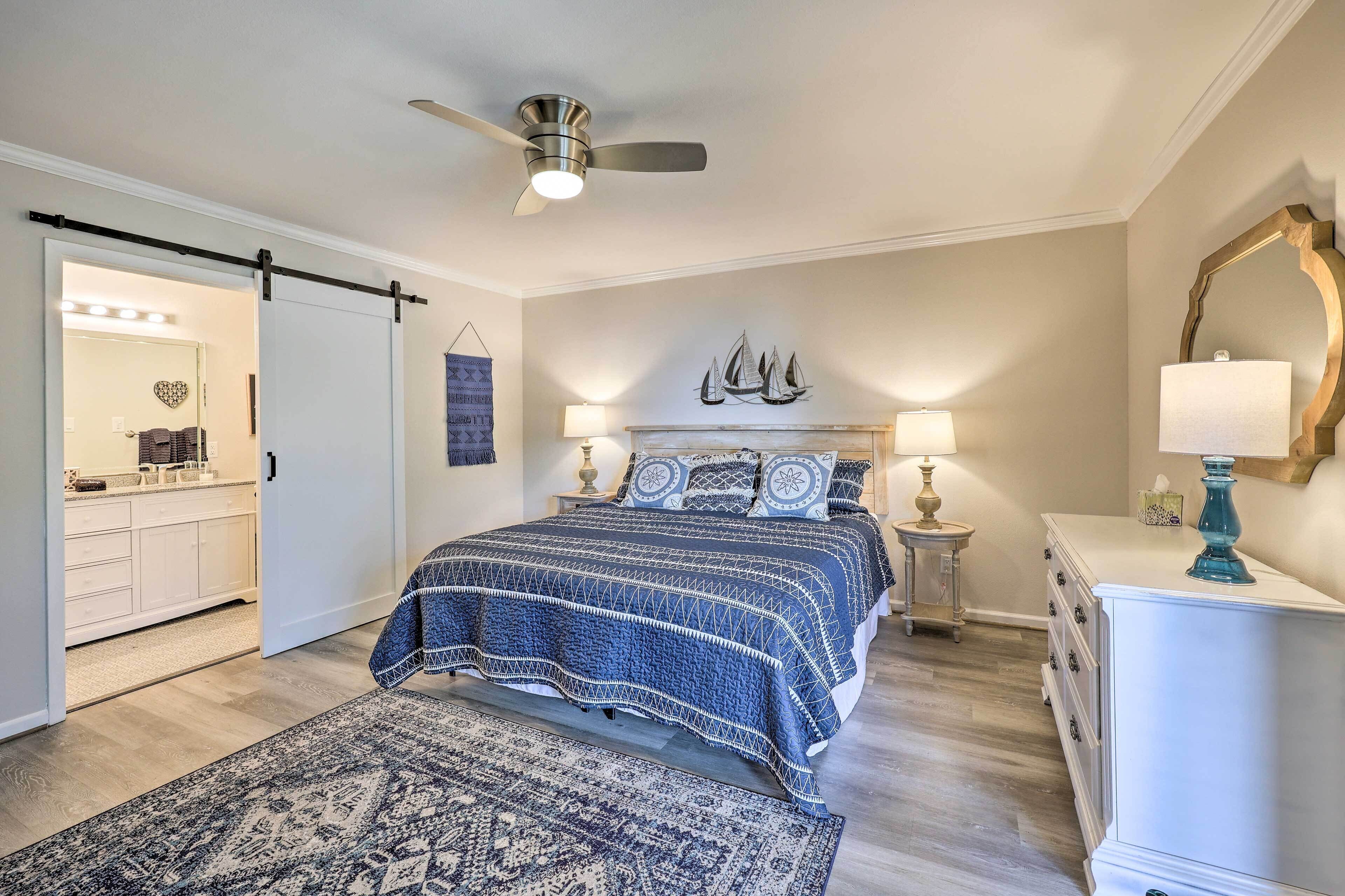 A bedroom with a bed, bedside tables, a dresser, a ceiling fan, and a wall with a decorative ship painting.