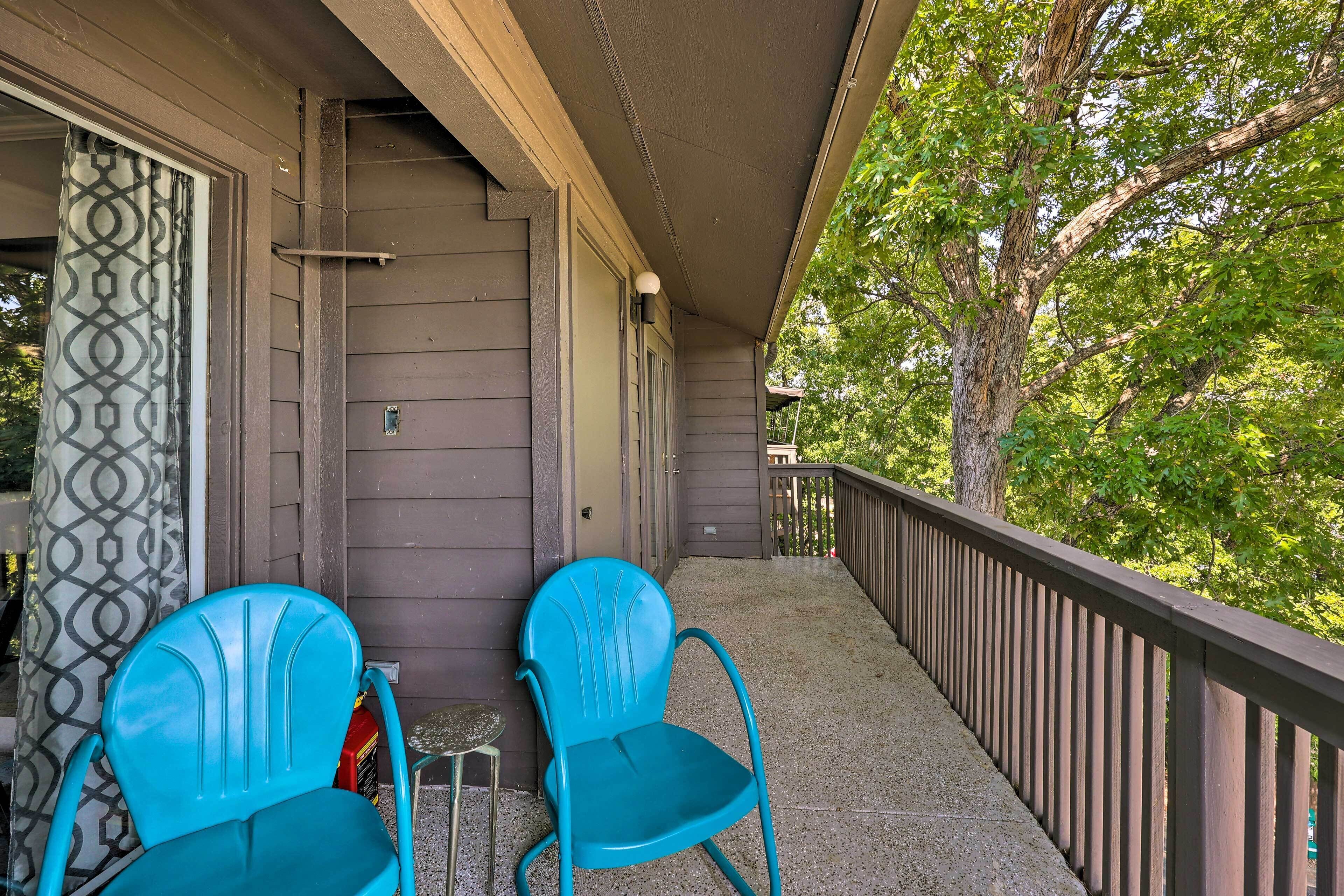 Une véranda avec deux chaises turquoise et une petite table, une balustrade en bois et une vue sur les arbres.