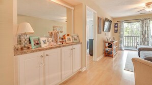 A spacious living area with a large mirror, a wooden floor, a sofa, and a balcony with curtains. - Pawleys Island Vacation Rental on Golf Course! (Pawleys Island)