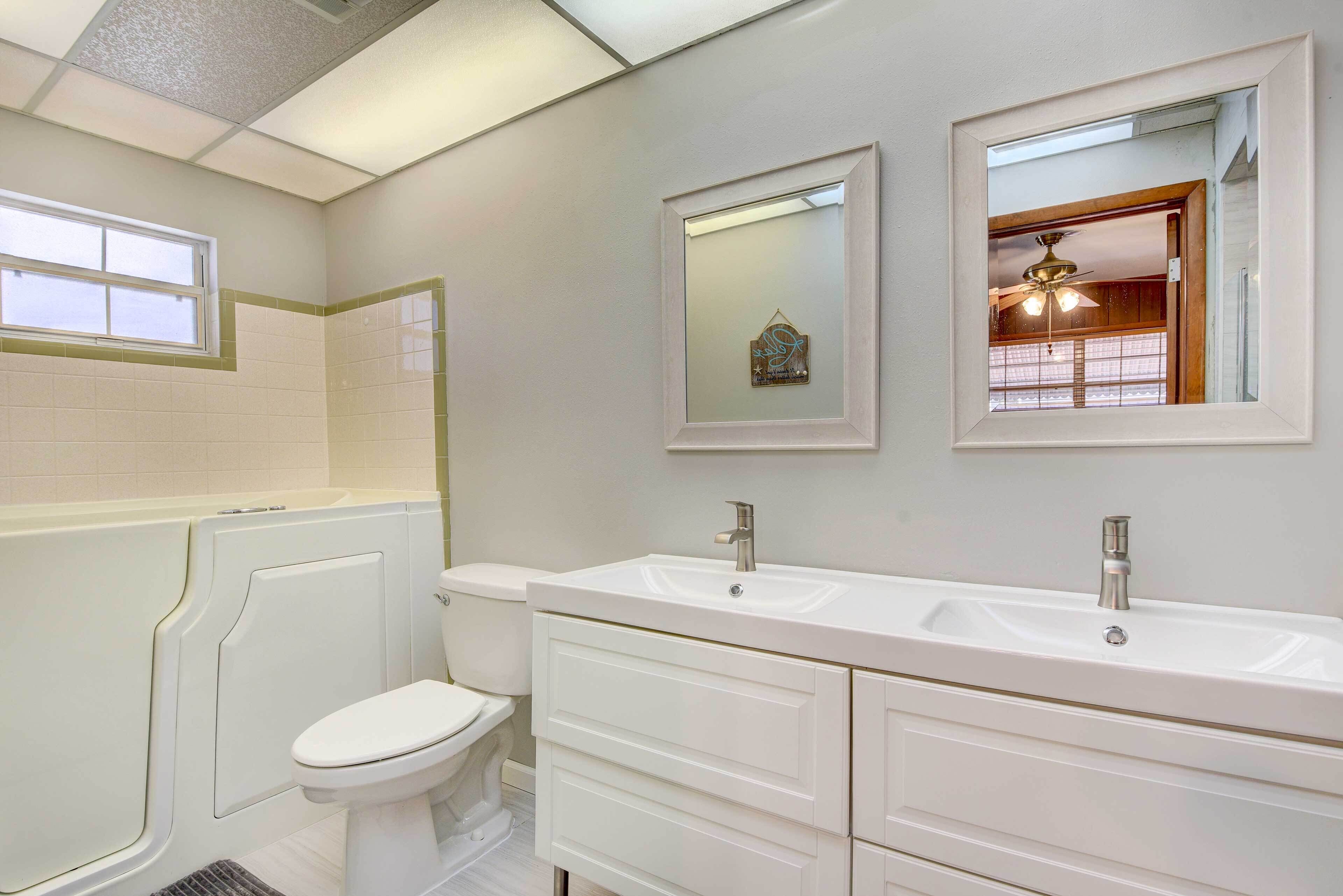 Un baño moderno con un tocador blanco, dos lavamanos, un inodoro y una ventana.