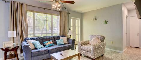 A living room with a blue sofa, a patterned armchair, a wooden coffee table, and a ceiling fan.