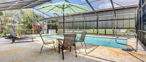 A covered outdoor area with a pool, lounge chairs, and a table with chairs.