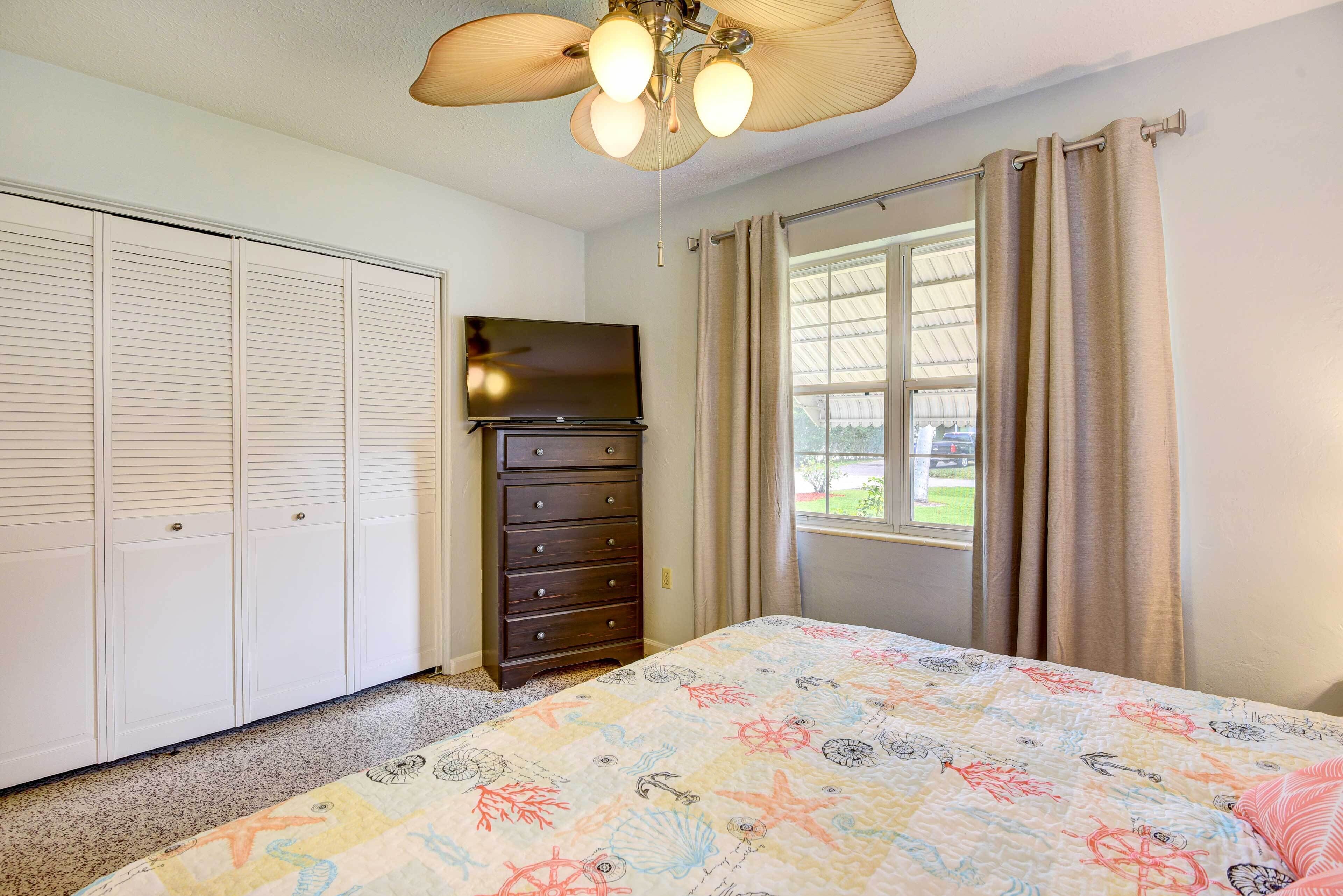 A bedroom with a bed, a dresser, a TV, a ceiling fan, and a window with curtains.