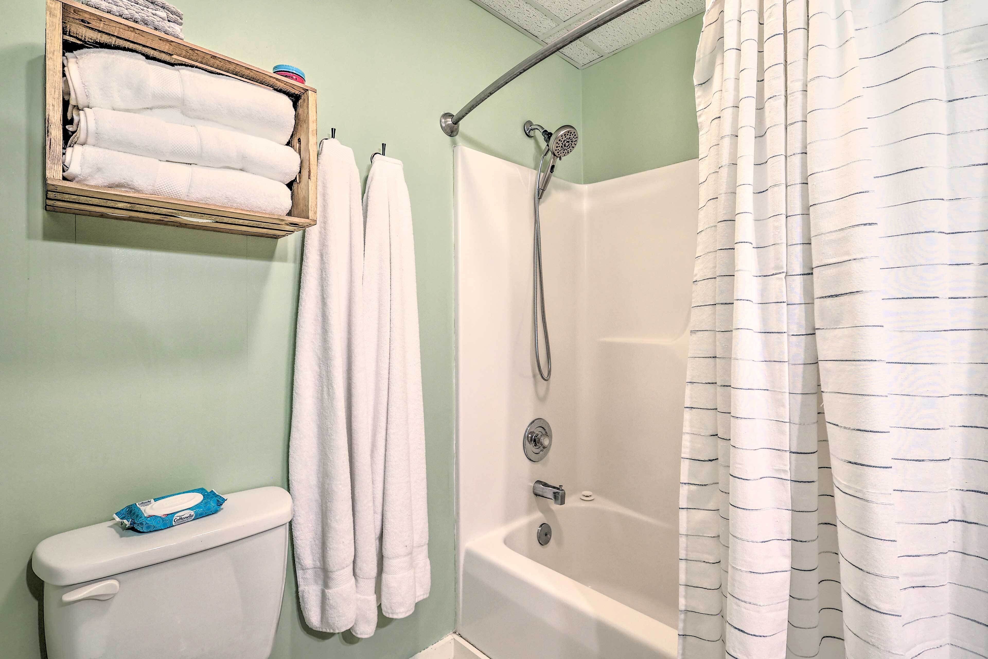 A bathroom with a shower, toilet, and a shelf with towels.