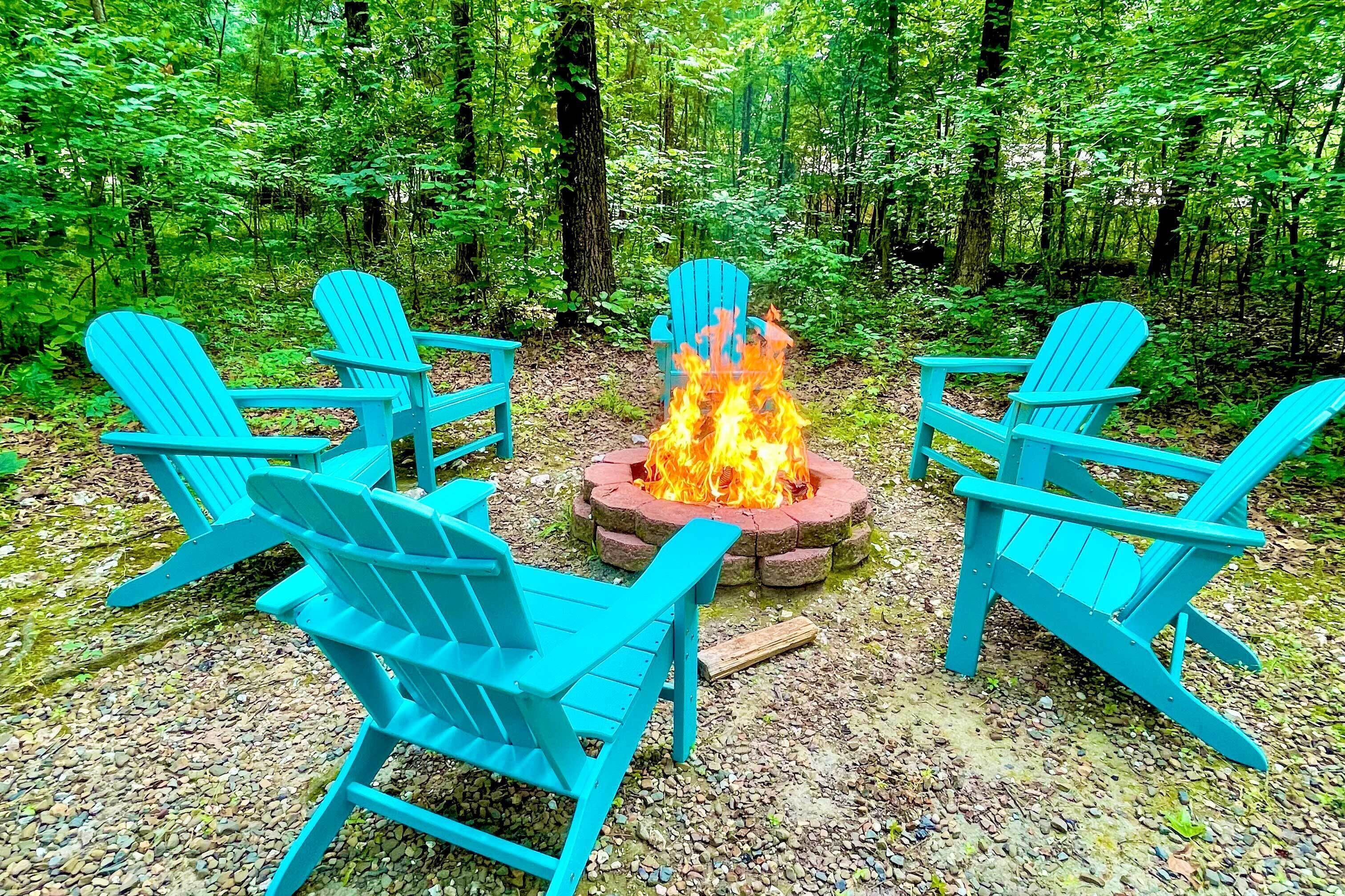Un paesaggio boschivo con un braciere e quattro poltrone Adirondack blu disposte attorno.