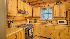 A wooden cabin-style kitchen with a stove, oven, microwave, sink, and wooden cabinets. - Broken Bow Cabin w/ Hot Tub, Near Hiking + Fishing (Broken Bow)