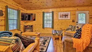 A cozy cabin interior with wooden walls, a television, a fireplace, and a couch with a blanket. - Broken Bow Cabin w/ Hot Tub, Near Hiking + Fishing (Broken Bow)