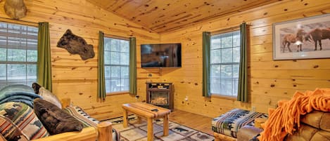 A log cabin interior with a fireplace, wooden furniture, and a mounted television.